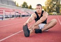 Young muscular athletic runner man stretching and touching his feet on a running court in sitting position before starting of Royalty Free Stock Photo