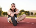 Young muscular athletic runner man stretching and touching his feet on a running court in sitting position before starting of Royalty Free Stock Photo