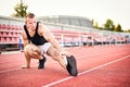 Young muscular athletic runner man stretching and touching his feet on a running court in sitting position before starting of Royalty Free Stock Photo