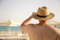 Young muscular attractive man in a hat looking at the sea. View from the back. Turquoise water and white sand. Vacation