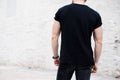 Young muscular bearded man wearing black tshirt and jeans posing in center of modern city. Empty concrete wall on the