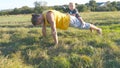 Young muscular father doing push ups with his little son on his back. Athletic man doing push-ups at green grass with