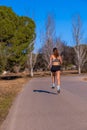 Young muscular female runner, dressed in tight shorts and top, mid-air running on an asphalt path through a mountain park Royalty Free Stock Photo