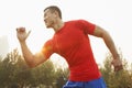 Young muscular man with a red shirt running and listening to music on earbuds outdoors in the park in Beijing, China Royalty Free Stock Photo