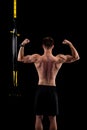 Young muscular man with trx loops isolated on black background, back view Royalty Free Stock Photo