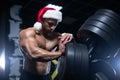 Young muscular Santa Claus in Christmas hat is having rest after working out training muscles in the gym standing next Royalty Free Stock Photo