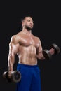 Young muscular sportsman is lifting heavy dumbbells showing his strong biceps isolated on black backgrounds Royalty Free Stock Photo