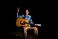 Young musician in plaid shirt playing the guitar and singing on dark background