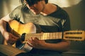 A young musician plays a tune on an old battered guitar, consulting the notes on a sheet of paper that lies on his knee Royalty Free Stock Photo