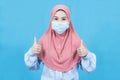 Young muslim asian woman with traditional dress wearing medical face mask under the outbreak of the virus,make gesture Thumbs up Royalty Free Stock Photo