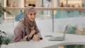 Young muslim businesswoman in hijab sitting in office at desk with laptop stirring coffee in paper cup leisure happy Royalty Free Stock Photo