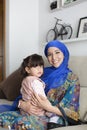 Young Muslim mother sitting on sofa with her little daughter in her arms. Single parent family life