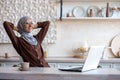 Young muslim woman freelancer in hijab sitting at table at home after working day using laptop. She threw her hands Royalty Free Stock Photo