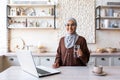 Young Muslim woman in hijab sitting at home in the kitchen with a laptop and holding a glass of pure mineral water Royalty Free Stock Photo