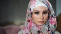 Young Muslim woman with painted eyes in hijab, looks at camera and blinks slowly