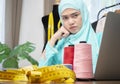 Young Muslim woman seller checking clothes details in store and writing data in computer labtop with a serious face Royalty Free Stock Photo
