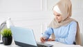 Young muslim woman student in hijab is doing her homework writing and drawing table on paper using laptop.