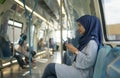 Young Muslim woman traveling inside subway train sitting while using phone.