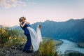 Young newly wed couple, bride and groom kissing, hugging on perfect view of mountains, river and blue sky Royalty Free Stock Photo