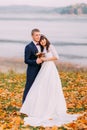 Young newlywed bridal couple holding each other on autumn lakeshore full of orange leaves Royalty Free Stock Photo