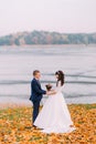 Young newlywed bridal couple posing on autumn lakeshore full of orange leaves Royalty Free Stock Photo