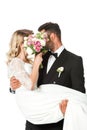 young newlyweds covering faces with bridal bouquet while groom carrying bride