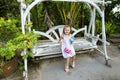 Young nice little girl riding on swing in exotic garden, palms in background.