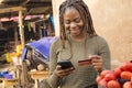 young nigerian woman selling in a local nigerian market using her mobile phone and credit card to do a transaction online smiling Royalty Free Stock Photo