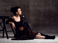 Young noble pregnant woman in black off-shoulder dress, leather jacket and boots sitting on floor and looking aside Royalty Free Stock Photo
