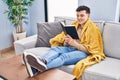 Young non binary man reading book sitting on sofa at home Royalty Free Stock Photo