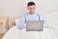 Young non binary man using laptop sitting on bed