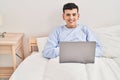 Young non binary man using laptop sitting on bed