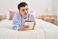 Young non binary man writing on notebook lying on bed