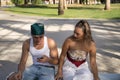 Young, non-conformist Latino and Hispanic boy and girl couple sitting on a bench checking social networks on their cell phone.