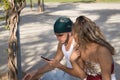 Young, non-conformist Latino and Hispanic boy and girl couple sitting on a bench checking social networks on their cell phone.