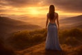 Young non recognizable woman with curvers in beautiful dress standing on top of hill at sunset and looks at that view