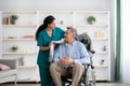 Young nurse covering disabled elderly man in wheelchair with warm plaid at retirement home Royalty Free Stock Photo