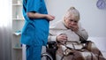 Young nurse giving medications to old lady in wheelchair, rehabilitation center Royalty Free Stock Photo