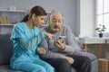 Young caregiver sitting on the sofa together with a senior man and helping him use his smartphone Royalty Free Stock Photo