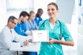 smiling young nurse holding tablet with colleagues sitting at table