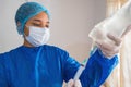 Young nurse with mask and hands in gloves preparing for medication administration, holding a syringe with liquid medicine of crown