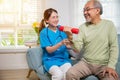 Young nurse physiotherapist helping old man in lifting dumbell at home Royalty Free Stock Photo