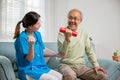 Young nurse physiotherapist support senior old man to lifting dumbell at home Royalty Free Stock Photo