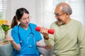 Young nurse physiotherapist support senior old man to lifting dumbell at home Royalty Free Stock Photo