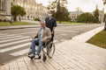 Young nurse in protective face mask assisting senior handicapped man in wheelchair during a walk in the city Royalty Free Stock Photo