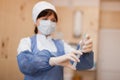 Young nurse in special sterile clothing in a protective mask is standing indoors holding a syringe in her hand. Royalty Free Stock Photo