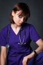 A young nurse with a stethoscope on his neck and work clothes is looking at his watch. Girl posing on a gray background