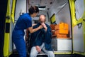 Young nurse in uniform puts oxygen mask on man sitting in blanket in the ambulance car