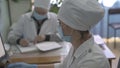 Young nurse works with a computer in foreground. Work of doctors team in ophthalmologist office. Mature female doctor