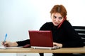 Young office worker woman talking on a cell phone sitting behind working desk with laptop computer and notebook Royalty Free Stock Photo